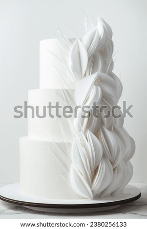 Big three tier wedding cake with white chocolate icing decorated with flowers made of edible wafer paper. White background Royalty-Free Stock Photo #2380256133