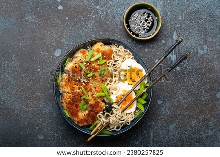 Asian noodles ramen soup with deep fried panko chicken fillet and boiled eggs in ceramic bowl with chop sticks, soy sauce on stone rustic background top view Royalty-Free Stock Photo #2380257825