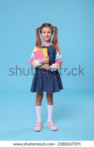 Happy schoolgirl with books on light blue background Royalty-Free Stock Photo #2380267591