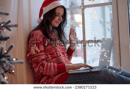 A young beautiful woman communicates via video call on a laptop from home near the window on the windowsill. Online Christmas concept. winter and warmth