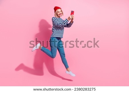 Full length photo of funky cute girl dressed striped shirt jumping texting messages modern device empty space isolated pink color background