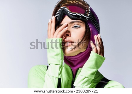 portrait of woman in active wear with balaclava on head posing on grey backdrop, hands near face Royalty-Free Stock Photo #2380289721
