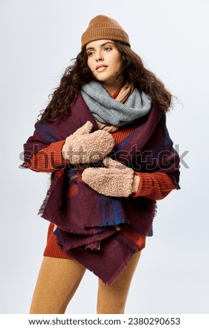 cozy layers, brunette woman in layered clothes with warm scarf and mittens on grey backdrop