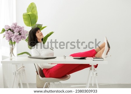 Elegant businesswoman closed eyes with legs on office table with laptop rests during break at work. Relaxed female boss in white shoes on heels sits at the desk, feels stress free. Work life balance.