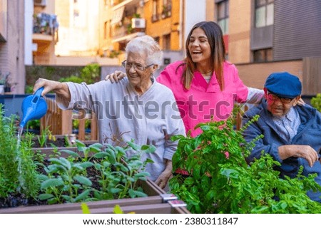 Happy retired elder people watering plants in a geriatric next to the supervision of a nurse Royalty-Free Stock Photo #2380311847