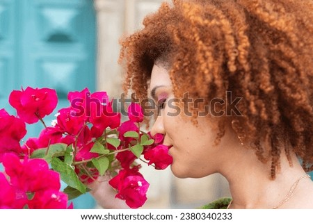 Close-up portrait of a red-haired woman's face with her eyes closed smelling a flower close to her nose. Confident and calm person.