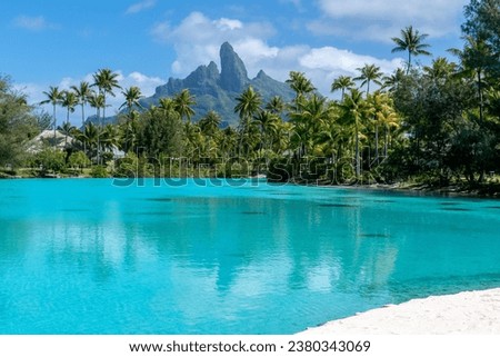Mt. Otemanu on Bora Bora, Tahiti in French Polynesia as seen from the palm-fringed lagoonarium at the St. Regis Resort. White sand beach fronts the spa behind, where couples massages are a specialty. Royalty-Free Stock Photo #2380343069