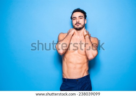 relaxed handsome man with beard standing shirtless on blue background holding his neck with hands