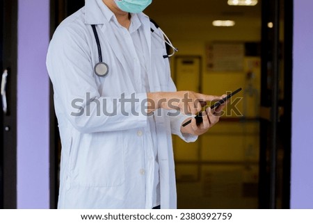 The doctor physician in white uniform with stethoscope using smartphone, standing in medical office, nurse or therapist typing and looking at phone screen