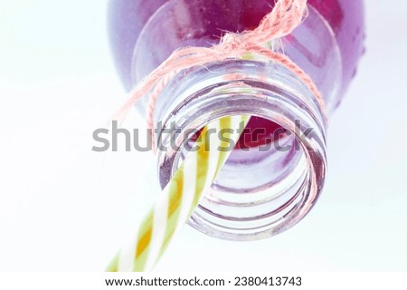 Glass bottle juice and yellow straw. Drink, concoction in an open bottle, with a thick orange thread bow. Soft drink, it can be diet or sugary, burgundy red. Liquid in glass bottle isolated on white Royalty-Free Stock Photo #2380413743