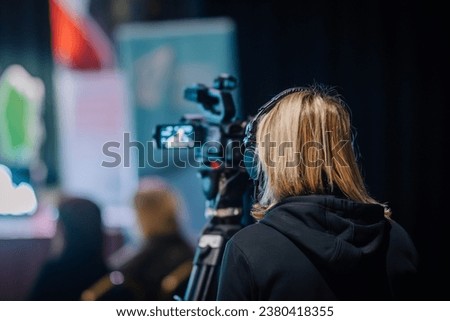 Valmiera, Latvia - October 20, 2023 - With a soft focus through the video camera's lens, the videographer is seen in a close-up shot, while a skilled woman operator operates the equipment 