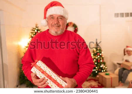 Happy man holding  gift box with smile hild wearing Chrismas jumper posing on floor near fireplace and xmas tree.