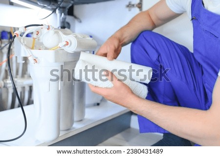 Plumber installs or change water filter. Replacement aqua filter. Repairman installing water filter cartridges in a kitchen. Installation of reverse osmosis water purification system Royalty-Free Stock Photo #2380431489