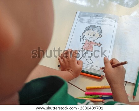 top view little boy drawing on paper sheet with colour pencils at home