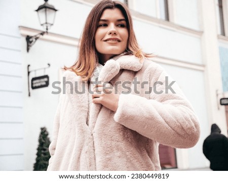 Young beautiful smiling lady wearing trendy white faux fur coat. Stylish woman posing in the street in winter. Cheerful and happy model in. Cold autumn weather. Shopping mall 