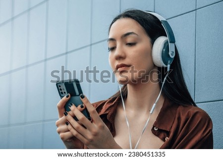 relaxed young woman with headphones and phone on blue wall
