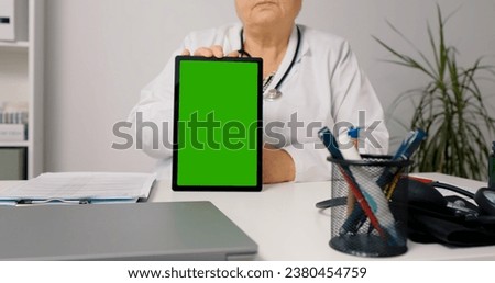 Woman doctor holds green screen mockup vertical tablet on the desk in office. Telemedicine concept female doctor use green screen tablet pc to see the patient and give advice.