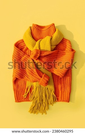 Knitted orange sweater with scarf on yellow background. Women's warm jumper, stylish autumn or winter clothes. Fashion autumnal outfit. Cozy bright  fall look. Flat lay, top view. Royalty-Free Stock Photo #2380460295
