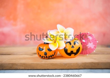 Plumeria flower with Halloween pumpkin and paper umbrella with space on orange cement wall, tropical Halloween card background idea
