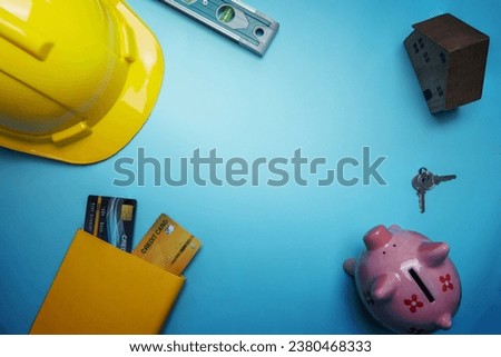 flat lay, top view of construction or business real estate concept with yellow helmet and small wooden house and credit card for buying property, home, building tools on blue background