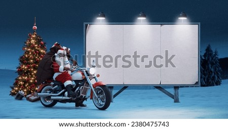 Unconventional Santa riding a motorcycle and blank advertising board, Christmas advertising campaign concept Royalty-Free Stock Photo #2380475743