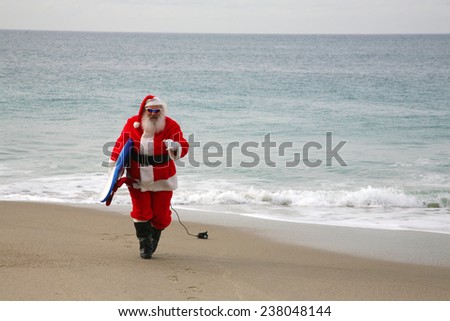 Surfing Santa Claus. Santa Claus holds his Blue Surfboard under his arm as he checks out the Waves at one of his Favorite Secret Surfing Spots. Santa loves Sports and Surfing. They call him Mr. Claus 