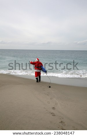Surfing Santa Claus. Santa Claus holds his Blue Surfboard under his arm as he checks out the Waves at one of his Favorite Secret Surfing Spots. Santa loves Sports and Surfing. They call him Mr. Claus 