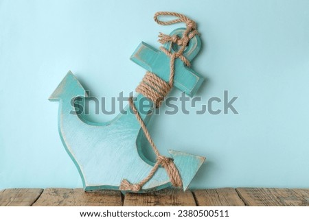 Anchor with hemp rope on wooden table near turquoise wall