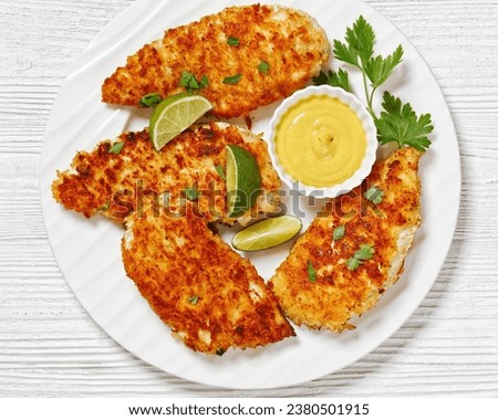 fried chicken cutlets under breadcrumbs and parmesan cheese crust on white plate with mustard and lime on white wooden table, horizontal view from above, flat lay, close-up Royalty-Free Stock Photo #2380501915