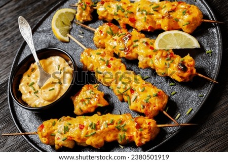 close-up of Bang Bang Chicken Skewers sprinkled with chives and lemon slices on black plate on dark wooden table, dutch angle Royalty-Free Stock Photo #2380501919