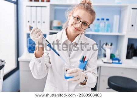 Young blonde woman scientist smiling confident pouring liquid on test tube at laboratory