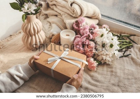 Gift box in hands with flowers at home.