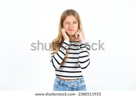 caucasian kid girl wearing striped T-shirt covering ears with fingers with annoyed expression for the noise of loud music. Deaf concept. Royalty-Free Stock Photo #2380511933