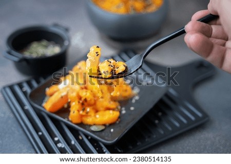 Close-up of baked pumpkin pieces on a fork. Pieces of pumpkin on a black flat plate on a wooden background. Healthy vegetarian, vegan food.