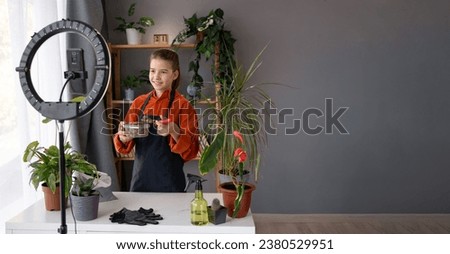 Young girl creator recording online media video on her room about transplant houseplants. Teenager streaming online and sharing social media content by mobile phone. Copy space. Banner Royalty-Free Stock Photo #2380529951