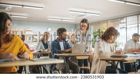 Young Teacher Checking Up on an Indian Man with Laptop Computer, Helping Him with a Task, Complimenting His Work. Modern Adult Training Center Help People to Develop New Useful Skills Throughout Life Royalty-Free Stock Photo #2380531903
