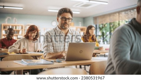 Middle-Aged Man Studying in Classroom, Using Laptop to Write Down Lecture Notes. Group of People Taking a Workshop on Improving Professional Soft Skills. Adult Education Center Concept Royalty-Free Stock Photo #2380531967