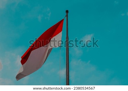 Photo of a vintage Indonesian flag “bendera merah putih” flying proudly over a mountain with a blue sky background