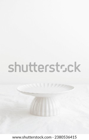 Empty tableware - white plate cakestand on white table as a background for a dessert vertical photo with a copy space Royalty-Free Stock Photo #2380536415