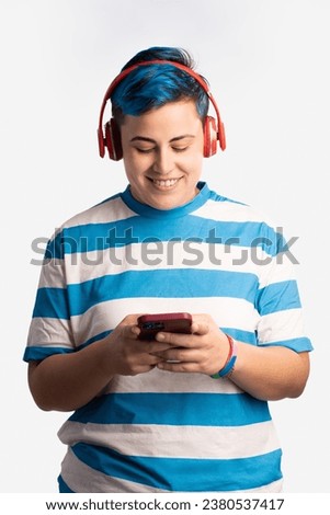 Gay woman enjoying music - Non-binary person with vibrant blue hair, wearing headphones, listens to music on their smartphone, displaying a peaceful and contented expression.