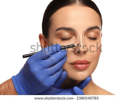 Woman preparing for cosmetic surgery, white background. Doctor drawing markings on her face, closeup Royalty-Free Stock Photo #2380540785