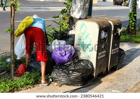 Rear view of old scavenger woman collecting used good around the trash bin in the city road side