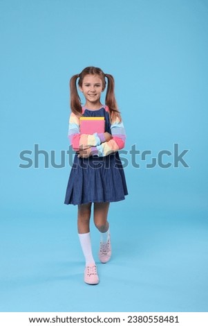 Happy schoolgirl with books on light blue background Royalty-Free Stock Photo #2380558481