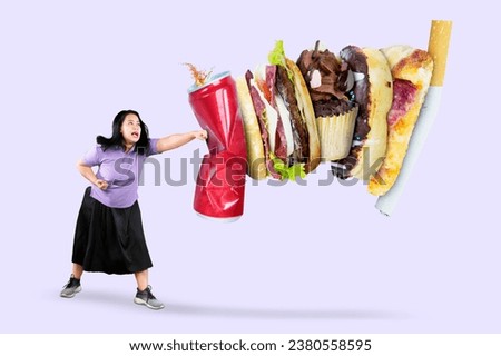 Picture of beautiful fat woman punching soft drink and fast food, isolated on grey background