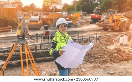 Female site engineer surveyor working with theodolite total station EDM equipment on a building construction site outdoors toned image