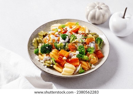 Autumn pasta salad with roasted pumpkin, broccoli, feta cheese on bright light gray background, vivid colors fall season salad, autumn food concept, top view