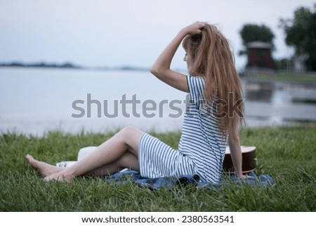 Young woman sitting at the beach by the lake on a cloudy day, touching her hair.