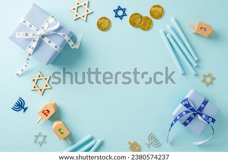 Festival of Lights: Overhead image featuring Star of David, menorah signs, gelt, trendy gift boxes, candles and dreidel on a pastel blue background, circular space perfect for text or advertising
