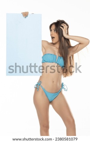 Young woman in bikini holding a advert empty board, isolated on white.