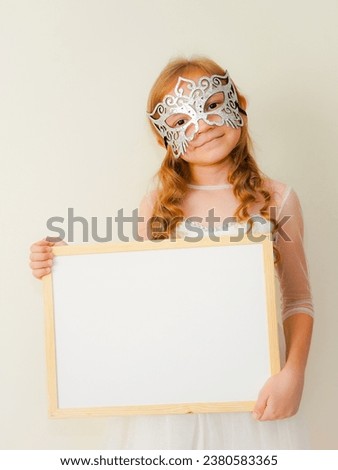 The Snow Queen.  Child in the form of a snow queen.  Little cute girl in a mask smiles and grimaces on a beige background. Child in masquerade carnival mask 